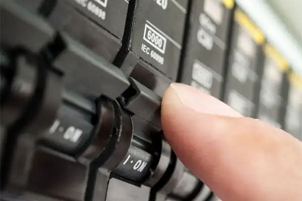 A close-up of a hand flipping a switch on an electrical circuit breaker panel.