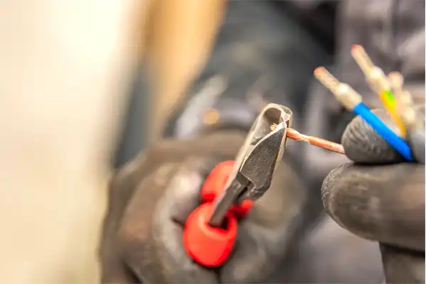 A person wearing gloves uses wire cutters to trim the end of an electrical wire.